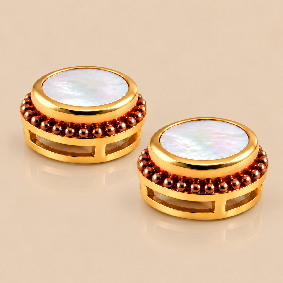 A pair of oval stud earrings with iridescent mother-of-pearl centers, surrounded by a gold inner ring and a textured rose gold plated outer bezel, set against a solid beige background.