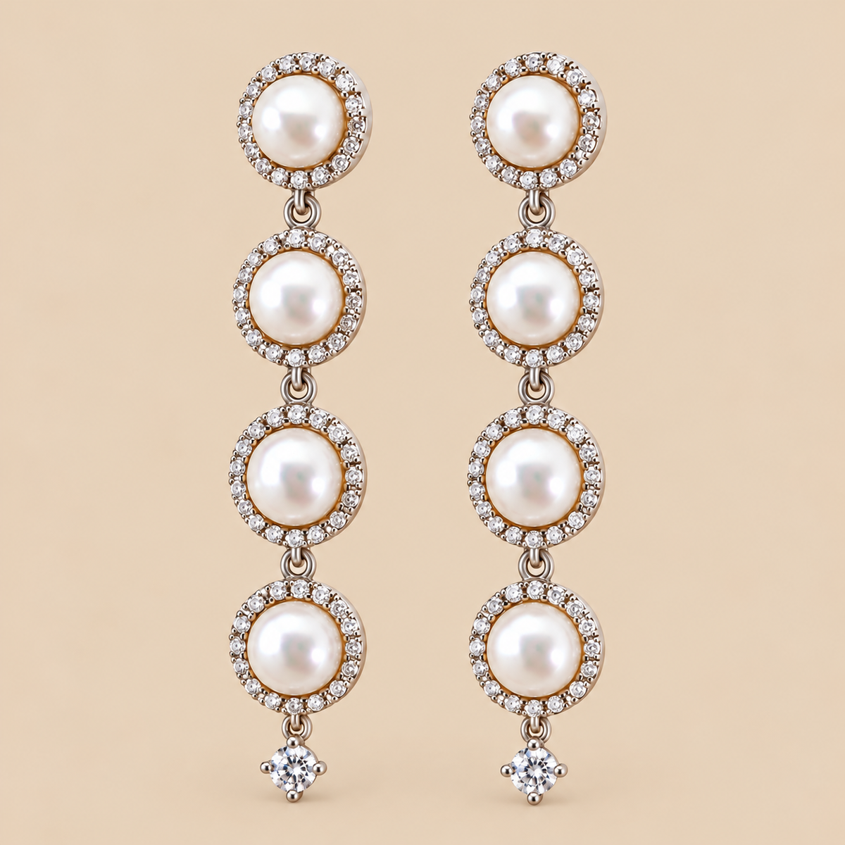 A pair of long drop earrings featuring four stacked white pearls in circular settings surrounded by small clear stones, with a single clear round-shaped stone dangling below each earring, shown on a solid beige background.