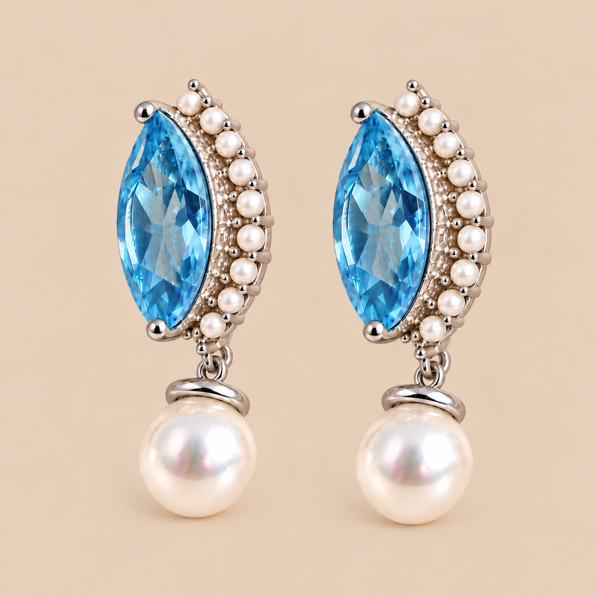 A pair of drop earrings featuring marquise-cut swiss blue topaz surrounded by small white pearls and silver-toned beads, with round white pearl drops below, set against a solid beige background.