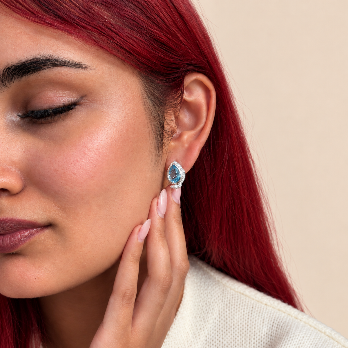 Teardrop-shaped earrings featuring swiss blue topaz gemstones, surrounded by clear pavé stones and accented with small white pearls, set in a silver-toned metal 