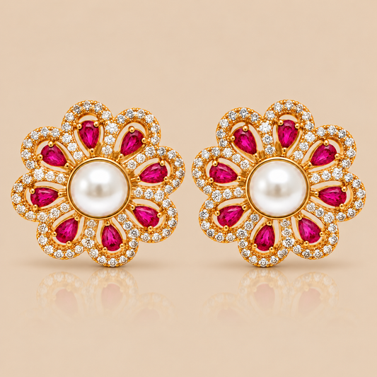 A pair of gold flower-shaped stud earrings with white pearl centers, surrounded by rows of small clear stones and bright pink teardrop-shaped gemstones, shown on a warm beige background.