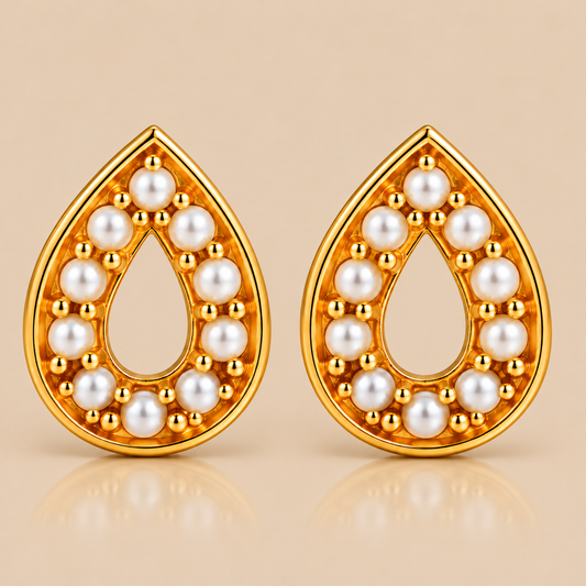A pair of gold teardrop-shaped earrings with white pearl accents, displayed on a warm beige background with a soft reflection below.